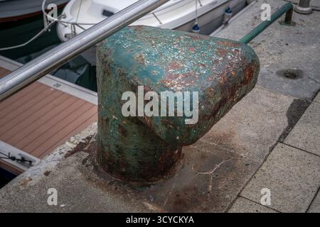 Borne d'amarrage en métal de couleur sarcelle fortement rouillée boulonnée à une jetée en béton dans une marina tranquille, montrant des signes d'altération et de décomposition Banque D'Images