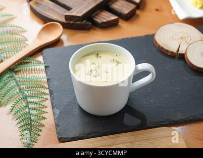 Soupe crémeuse de maïs en tasse blanche servie sur planche de bois avec cuillère vue latérale de la nourriture taïwanaise Banque D'Images