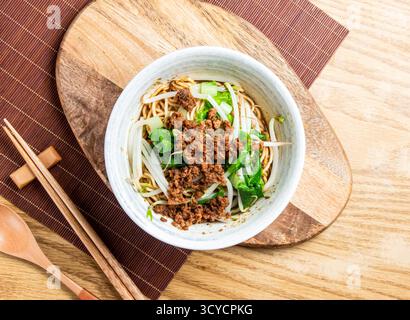Dan Dan nouilles avec porc moulu dans une sauce au sésame servi dans un bol avec des baguettes et une cuillère isolé sur planche de bois vue latérale de la nourriture de taiwan Banque D'Images