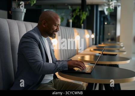Vue latérale de l'homme d'affaires mûr souriant dans le travail décontracté intelligent sur ordinateur portable dans le salon de bureau Banque D'Images