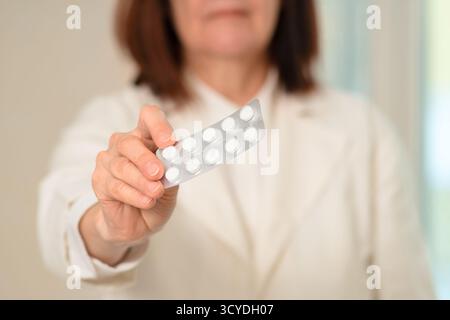 Une femme médecin dans un manteau médical tient des comprimés dans sa main ouverte. Gros plan montrant les soins et l'expertise dans le traitement des patients. Met l'accent sur la confiance, les solutions de santé et la responsabilité professionnelle. Banque D'Images