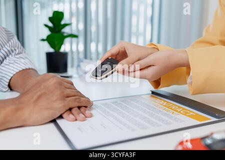 Une négociation de vente de voitures a lieu dans un bureau où une vendeuse dans un blazer jaune explique les détails d'un contrat à un client masculin, Showin Banque D'Images