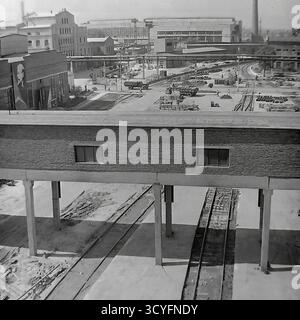 Cette photo d'archives en noir et blanc des années 1970 donne une vue en grand angle de l'armature-isolant Slavyansk (AIZ) à Sloviansk, URSS. La photo donne sur une grande passerelle couverte surélevée (pont piétonnier) qui traverse plusieurs voies ferrées en contrebas. En arrière-plan, la vaste cour d'usine est visible, animée de camions, de travailleurs et de zones de stockage de produits. Un grand portrait de Vladimir Lénine est bien visible sur le mur d'un atelier. Cette image montre l'infrastructure complexe d'un site industriel soviétique majeur Banque D'Images