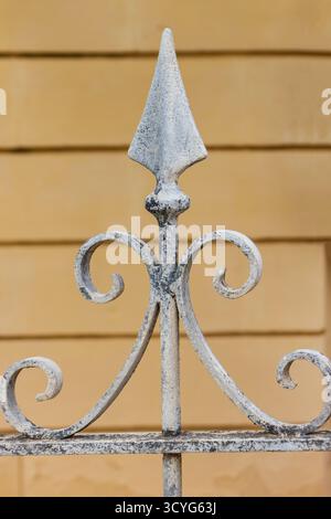 Finition de clôture décorative en fer forgé avec volutes et pointes de lance contre mur jaune Banque D'Images