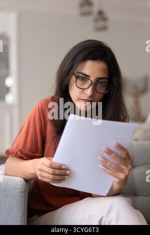 Femme latine anxieuse sérieuse dans des lunettes lisant un document papier Banque D'Images