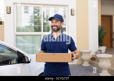 Travailleur souriant du service de livraison debout près de la boîte de retenue de voiture Banque D'Images