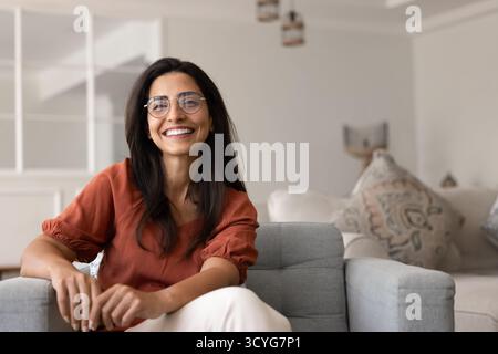 Jeune femme hispanique joyeuse dans des lunettes élégantes assis dans un fauteuil Banque D'Images