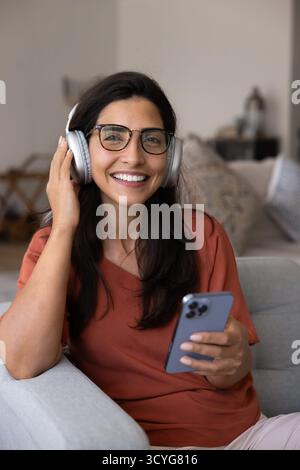 Heureuse belle femme latine portant des lunettes tendance et de gros écouteurs Banque D'Images