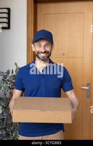 Joyeux livreur en uniforme posant à la boîte de maintien de porte Banque D'Images