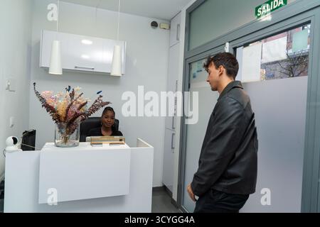 Homme arrivant à la réception avec réceptionniste femme attendant dans un hall de la clinique Banque D'Images