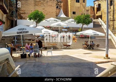 Bormla, Malte – 07.13.2025 : un café en plein air avec des parasols Somersby et des décorations en forme de cœur sur les marches de la place ensoleillée de la vieille ville Banque D'Images