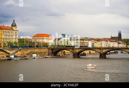 Prague Vltava rivière avec pont de pierre historique, bâtiments colorés au bord de la rivière, architecture baroque, bateaux, flèches jumelles de Vysehrad à distance, ensoleillé Banque D'Images
