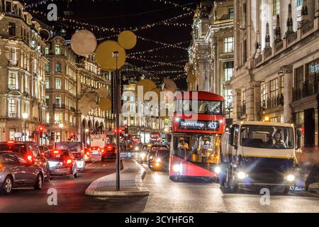 Bus rouge à impériale traversant une rue festive de Londres la nuit avec des lumières de Noël, des gens faisant du shopping et des vitrines illuminées pendant le Banque D'Images