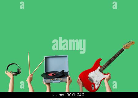 Mains féminines avec lecteur de disque vinyle vintage, guitare électrique, baguettes de batterie et écouteurs sur fond vert Banque D'Images