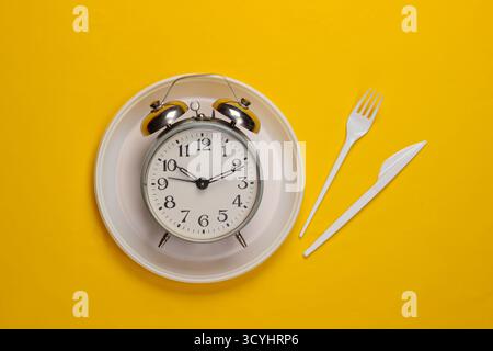 Heure du pique-nique. Réveil dans une assiette avec une fourchette et un couteau jetables. Vue de dessus Banque D'Images