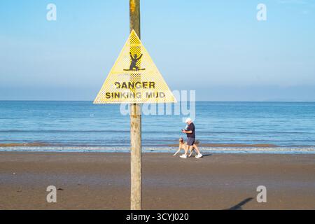Danger couler panneau d'avertissement de boue sur la plage avec promeneur de chien à Weston-super-Mare Banque D'Images