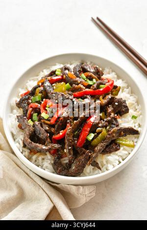 Bœuf au piment croustillant de style asiatique en sauce piment sucrée et épicée avec riz basmati dans un bol blanc sur fond de pierre claire. Vue rapprochée Banque D'Images