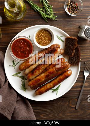 Assiette avec de délicieuses saucisses fines grillées sur une table en bois brun. Vue de dessus, pose à plat Banque D'Images