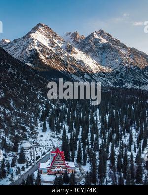 Un pavillon de montagne au toit rouge entouré de pins poussiéreux de neige sur fond de montagnes accidentées, ensoleillées et enneigées et d'un ciel bleu Banque D'Images