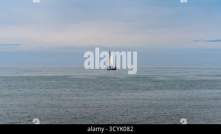 Un seul petit voilier traditionnel vu de loin sur une mer calme. Pris sur un jour d'automne partiellement nuageux sans personne. Banque D'Images