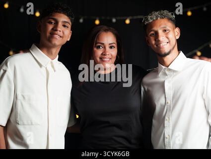 Une femme et deux jeunes hommes sourient à la caméra. La femme porte une chemise noire et les hommes portent des chemises blanches Banque D'Images