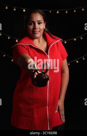 une femme vêtue de rouge posant pour une photo avec un fond noir et un gâteau à la main Banque D'Images