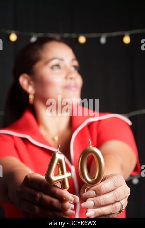 Une femme tient deux bougies, dont l'une porte le numéro 40. Elle porte une chemise rouge Banque D'Images
