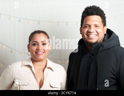 Un homme et une femme sourient à la caméra. La femme porte une chemise blanche et l'homme porte un sweat à capuche noir Banque D'Images