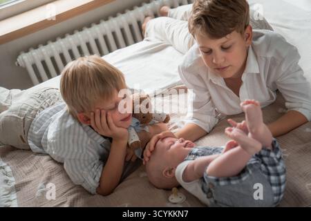 Trois frères passent du temps ensemble à la maison, allongés sur le lit et jouant avec leur frère et sœur Banque D'Images