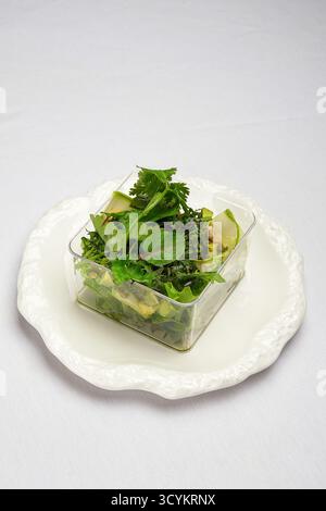 salade verte fraîche, légumes frais mélangés et herbes servis dans un récipient portable en plastique sur assiette blanche Banque D'Images