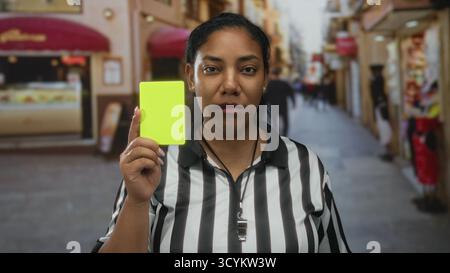 Arbitre femme avec l'expression sérieuse tient le carton jaune vers le haut avec la main tendue sur la rue de la ville ; jugement officiel. Banque D'Images