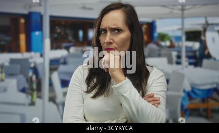 Femme contemplant à l'extérieur sur la terrasse du restaurant avec une expression réfléchie sous un ciel ensoleillé indiquant une ambiance de rue vibrante et animée autour Banque D'Images