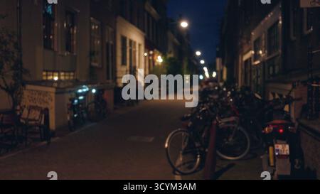 Rue de ville nocturne avec des lumières défocalisées et des vélos dans une ville européenne, créant une scène urbaine atmosphérique avec une architecture floue et une ruelle. Banque D'Images
