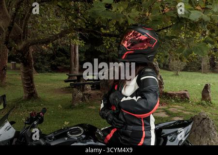 Femme motard portant un équipement de protection complet assis sur une moto dans un parc Banque D'Images