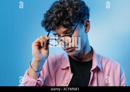Teen abaisse les lunettes tout en pensant à un examen de la vue, montrant une mauvaise vue, le choix de prescription et l'optométrie moderne dans une scène de studio propre. Banque D'Images