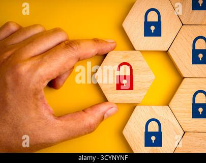 Concept de cybersécurité montrant un cadenas rouge déverrouillé placé à la main parmi les icônes verrouillées sur des hexagones en bois connectés. Symbole de violation de données, piratage ri Banque D'Images
