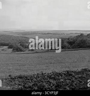 Cette photo d'archive des années 1970 montre une vue panoramique à angle élevé époustouflante du paysage rural près de Mayaky, oblast de Donetsk, RSS d'Ukraine. La photo donne sur de vastes champs agricoles et des collines ondulantes. Au premier plan, la terre sombre et fraîchement labourée contraste avec une prairie herbeuse. Au loin, un petit village est visible, et au-delà, une grande étendue d'eau, probablement la rivière Siverskyi Donets, s'étend jusqu'à l'horizon. Cette image capture parfaitement la beauté pastorale et expansive de la campagne soviétique, un élément clé du Donbass paisible Banque D'Images