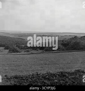 Cette photo d'archive des années 1970 montre une vue panoramique à angle élevé époustouflante du paysage rural près de Mayaky, oblast de Donetsk, RSS d'Ukraine. La photo donne sur de vastes champs agricoles et des collines ondulantes. Au premier plan, la terre sombre et fraîchement labourée contraste avec une prairie herbeuse. Au loin, un petit village est visible, et au-delà, une grande étendue d'eau, probablement la rivière Siverskyi Donets, s'étend jusqu'à l'horizon. Cette image capture parfaitement la beauté pastorale et expansive de la campagne soviétique, un élément clé du Donbass paisible Banque D'Images