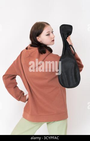 Vue arrière de la musicienne avec ukulélé dans sa main, tient l'instrument derrière son dos et regarde par-dessus l'épaule. Elle porte un sweat à capuche marron et gr léger Banque D'Images