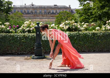 Danseuse de ballet en robe corail enfilant des chaussures pointe dans le jardin de Paris Banque D'Images