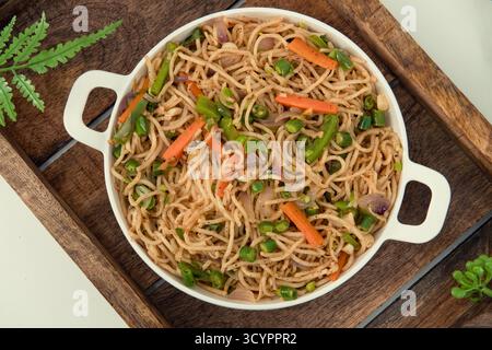 Savoureuses nouilles hakka aux légumes dans une assiette blanche et un fond isolé. Plat de cuisine végétarienne indo-chinoise. Nouilles végétales indiennes avec légumes. Banque D'Images