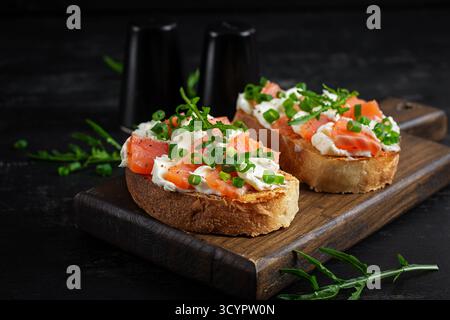 Sandwichs au saumon, poisson salé, fromage à la crème et oignon vert sur fond de bois. Petit déjeuner sain avec toasts de saumon Banque D'Images