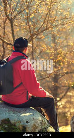 Un homme est assis sur une pierre au-dessus d'un beau lac de montagne par un jour ensoleillé d'automne. Bannière verticale Banque D'Images