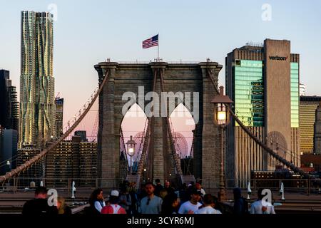 New York. 01 octobre 2025. - Les gens traversent le pont historique de Brooklyn pendant le lever du soleil, révélant une ligne d'horizon dynamique de Manhattan à New York. Banque D'Images