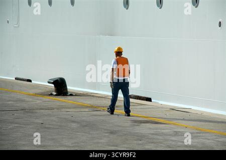 Dubrovnik. Croatie - 20 octobre 2025 : vue arrière d'un docker avec un casque de sécurité et un gilet de sécurité. L'homme marche sur une jetée en béton à côté du blanc Banque D'Images