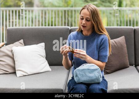 Femme tenant la bouteille d'huile essentielle assise sur le canapé Banque D'Images