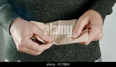 gros plan d'un homme dans un pull tricoté sur le point d'utiliser un mouchoir en papier recyclé, les deux mains l'étirant pour révéler sa surface unie Banque D'Images