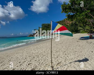 Drapeau des Seychelles agitant sur le sable blanc immaculé de la plage d'Anse Georgette, Praslin Banque D'Images