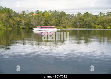 Bateau à passagers glissant sur un lagon réfléchissant entouré d'arbres dans un centre de villégiature à Orlando, en Floride Banque D'Images
