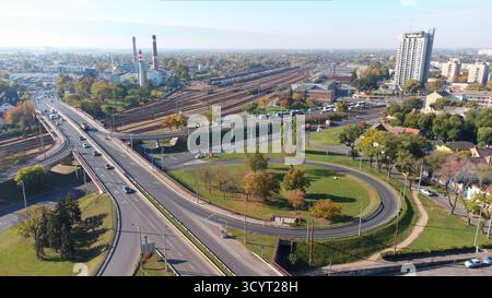 Vidéo de drone d'une zone urbaine avec un grand carrefour routier, rond-point et pont surélevé près d'une gare très fréquentée avec des trains de marchandises Banque D'Images